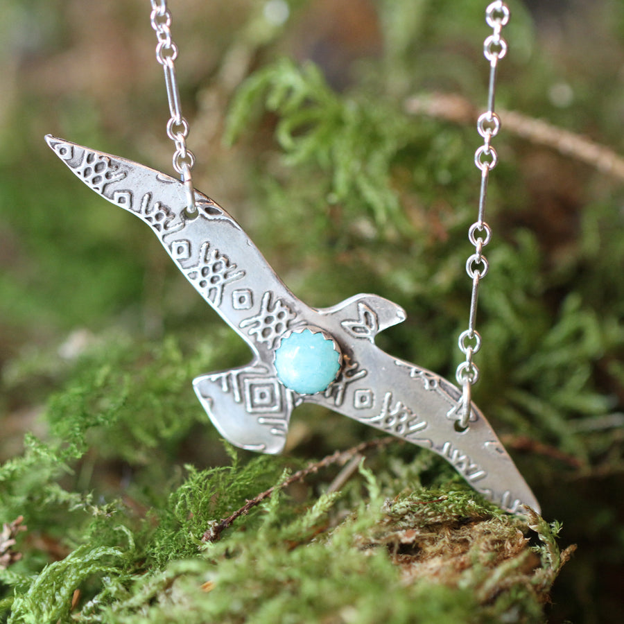 close up of flying bird pendant displayed upon green moss backdrop