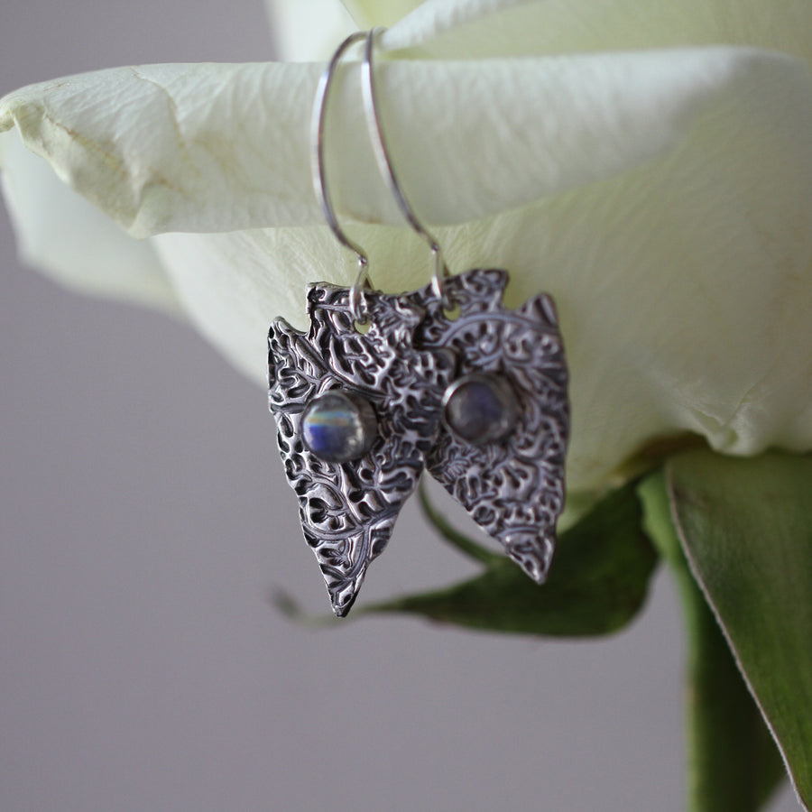 Handmade sterling silver arrowhead earrings hanging on the petal of a white rose